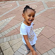 Bella joined the competition — help win amazing prizes! child, smiling, tshirt, outdoor, pavement, patterned_floor, grass, happy, sneakers, girl, casual_clothing, playful, portrait, daylight, curly_hair, young_person, concrete, pointing, cute, fun