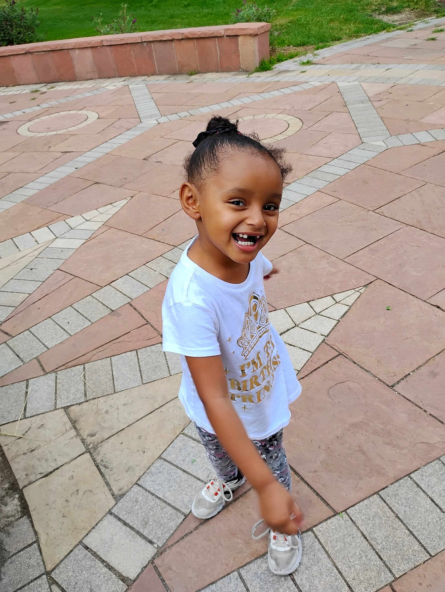 Bella joined the competition — help win amazing prizes! child, smiling, tshirt, outdoor, pavement, patterned_floor, grass, happy, sneakers, girl, casual_clothing, playful, portrait, daylight, curly_hair, young_person, concrete, pointing, cute, fun
