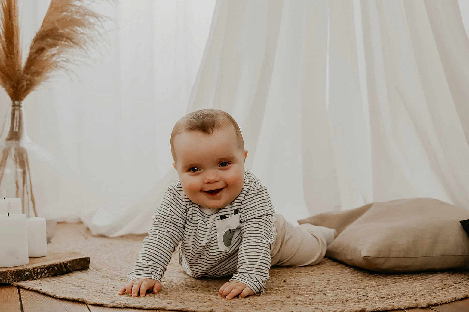 Jules a rejoint le concours — aidez-le/la à gagner de superbes lots ! baby, crawling, smile, striped_clothing, rug, pillow, candles, wooden_floor, vase, pampas_grass, curtains, indoor, child, portrait, happy, cozy, soft_light, floor, homedecor, infant