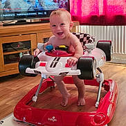 Sebastian joined the competition — help win amazing prizes! baby, child, curtain, floor, foot, furniture, happy, head, indoor, living_room, person, play, red, seat, smiling, television, toy_car, walker, white, wood_floor