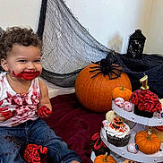 Owen is registered to the contest to win money with this photo: birthday_candle, cake, celebration, child, cupcakes, curly_hair, decorations, eyeballs, festive, fun, halloween, indoor, jeans, messy, pumpkins, red_frosting, smiling, spider, toddler, white_tank_top