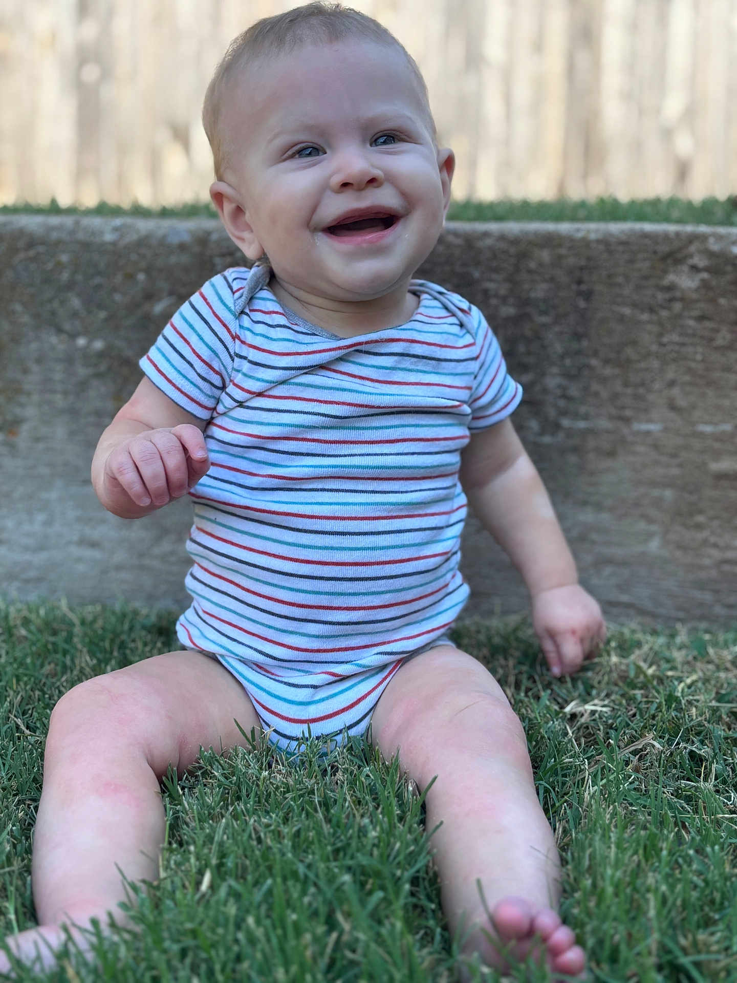 Kaysen is registered to the contest to win money with this photo: baby, child, grass, outdoor, smiling, happy, onesie, striped_clothing, barefoot, person, sitting, cute, infant, nature, young_child, daylight, face, skin, head, expression