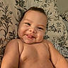 baby, infant, child, portrait, smiling, tongue_out, face, eyes, bare_shoulders, skin, lying_down, bed, pillow, floral_pattern, home, indoor, close_up, happy, adorable, photography