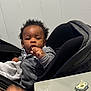 baby, child, stroller, pacifier, gray_hoodie, snack, table, indoor, curly_hair, black_stroller, hand, face, expression, seated, blanket, comfort, young_child, infant, casual, relaxed
