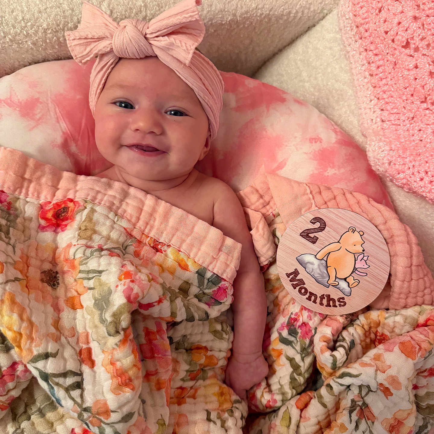 Vaeda is registered to the contest to win money with this photo: baby, smiling, headband, pink, blanket, floral, cushion, milestone_card, winnie_the_pooh, infant, cute, portrait, indoors, child, happy, soft_texture, wrapped, two_months, lying_down, cozy