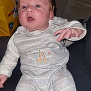 William joined the competition — help win amazing prizes! baby, infant, pajamas, giraffe, gray_clothing, person, face, hand, couch, fabric, indoor, seated, expression, holding, child, soft_lighting, casual, background, yellow_bag, cozy