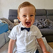Lyvio a rejoint le concours — aidez-le/la à gagner de superbes lots ! toddler, child, smiling, white_shirt, bow_tie, jeans, indoor, sofa, blanket, teddy_bear, wall_art, happy, laughing, person, home, furniture, cute, portrait, seated, cozy