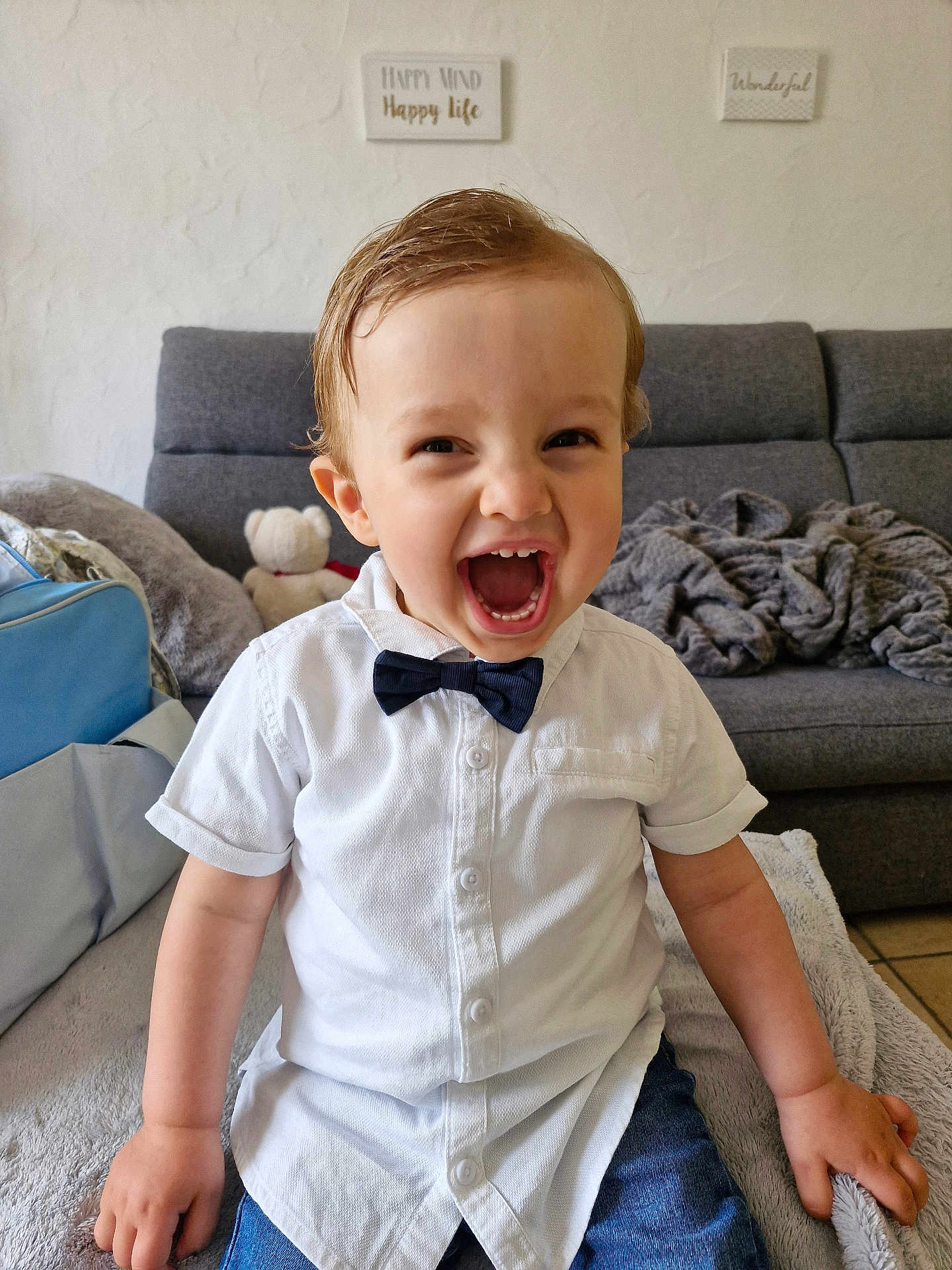 Lyvio a rejoint le concours — aidez-le/la à gagner de superbes lots ! toddler, child, smiling, white_shirt, bow_tie, jeans, indoor, sofa, blanket, teddy_bear, wall_art, happy, laughing, person, home, furniture, cute, portrait, seated, cozy