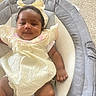 baby, baby_seat, carpet, child, clothing, comfort, cushion, cute, face, hand, headband, indoor, infant, legs, person, portrait, skin, smile, yellow_dress, young