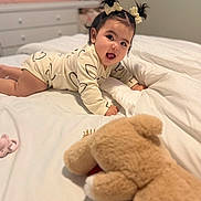 Celine is registered to the contest to win money with this photo: baby, infant, pigtails, hair_bows, onesie, bed, blanket, teddy_bear, pacifier, crawling, nursery, child, smiling, indoor, soft_toy, cute, sleepwear, furniture, happy, portrait