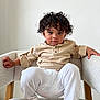 toddler, child, curly_hair, beige_shirt, white_pants, armchair, furniture, indoor, portrait, person, cute, baby, relaxed, seated, looking_at_camera, expression, skin, foot, hand, cozy