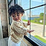 Niko joined the competition — help win amazing prizes! toddler, child, curly_hair, window, beige_shirt, white_pants, indoor, natural_light, looking_away, playful, curious, portrait, young_child, person, casual_clothing, daylight, blurred_background, hand_on_window, soft_texture, light
