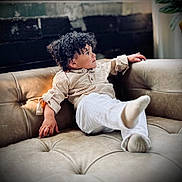 Niko joined the competition — help win amazing prizes! toddler, child, curly_hair, couch, indoor, relaxed, casual_clothing, beige, soft_lighting, portrait, young_child, furniture, home, sitting, cute, person, cozy, expression, comfort, skin