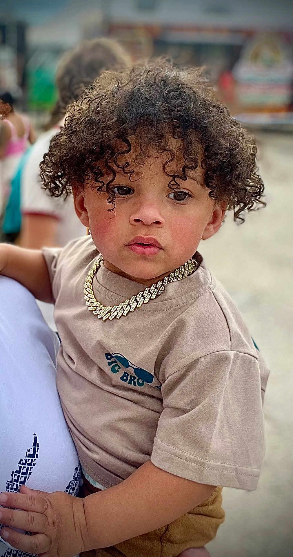 Niko is registered to the contest to win money with this photo: child, toddler, curly_hair, necklace, chain, tshirt, big_bro, hand, person, outdoor, blurred_background, serious_expression, holding, adult, skin, face, fashion, accessory, casual_clothing, portrait
