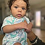 baby, infant, curly_hair, onesie, whale_pattern, hand, bracelet, indoor, blurred_background, portrait, child, cute, skin, face, eyes, mouth, person, holding, young, closeup