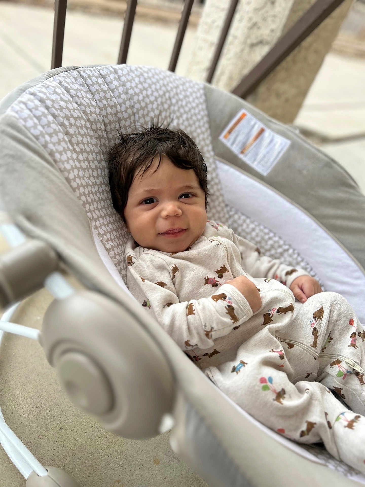 Josiah is registered to the contest to win money with this photo: baby, infant, child, smiling, onesie, baby_rocker, patterned_clothing, indoor, soft_focus, dark_hair, cute, comfortable, portrait, person, seat, fabric, cozy, happy, face, young_child