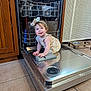 baby, child, dishwasher, kitchen, floor, tile, metal, cabinet, appliance, smiling, headband, clothing, curly_hair, cute, sitting, indoors, face, person, young_child, playful