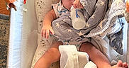 River is registered to the contest to win money with this photo: baby, baby_clothing, bassinet, blanket, bottle, child, colorful, cozy, cushion, drinking, family_photo, indoors, infant, lying_down, nursery, play_gym, portrait, sleeping_area, star_pattern, toy
