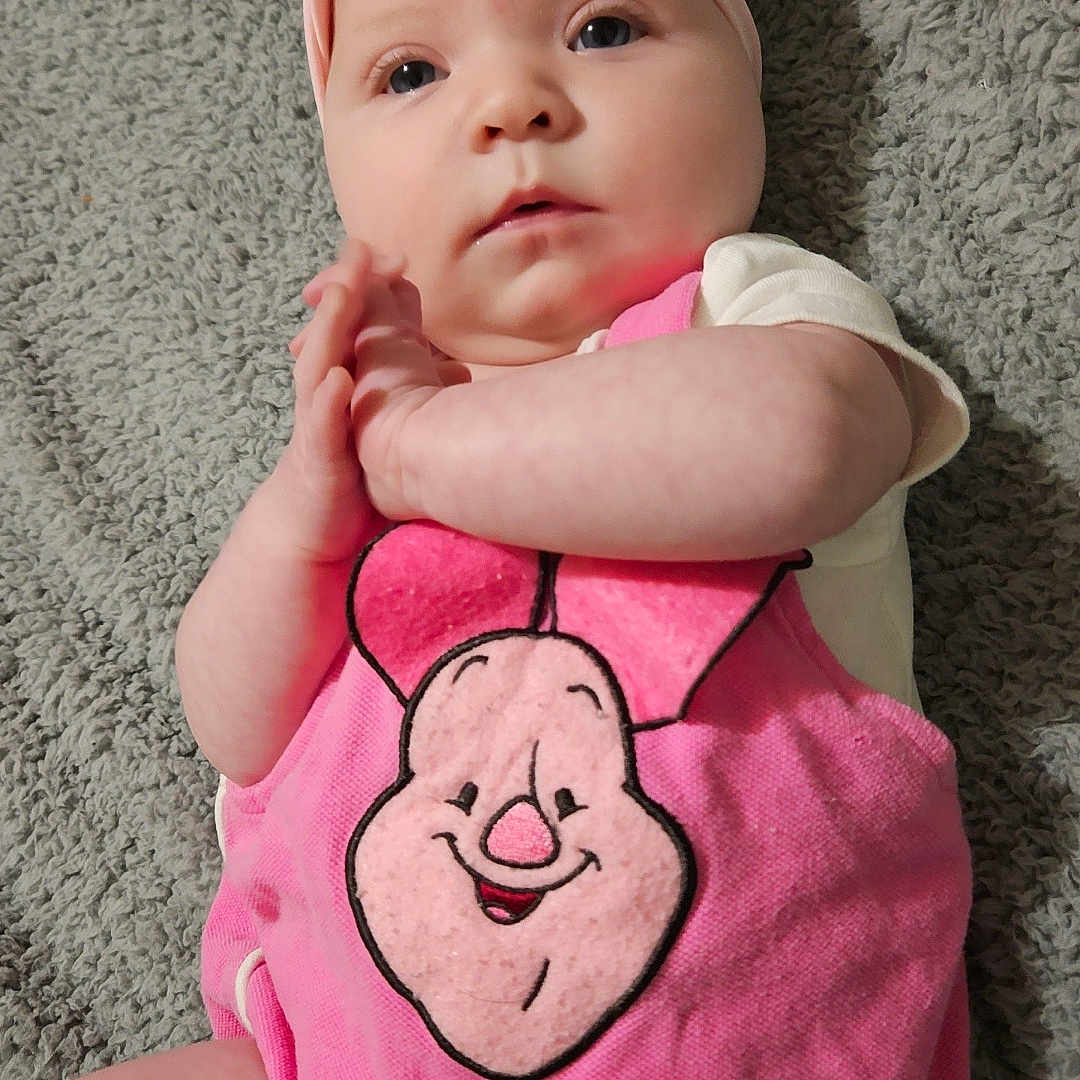 Willow is registered to the contest to win money with this photo: adorable, baby, blanket, cartoon_face, child, closeup, clothing, cute, expression, hands_clasped, headwear, indoor, infant, lying_down, pink_headband, pink_outfit, portrait, skin, soft_texture, young