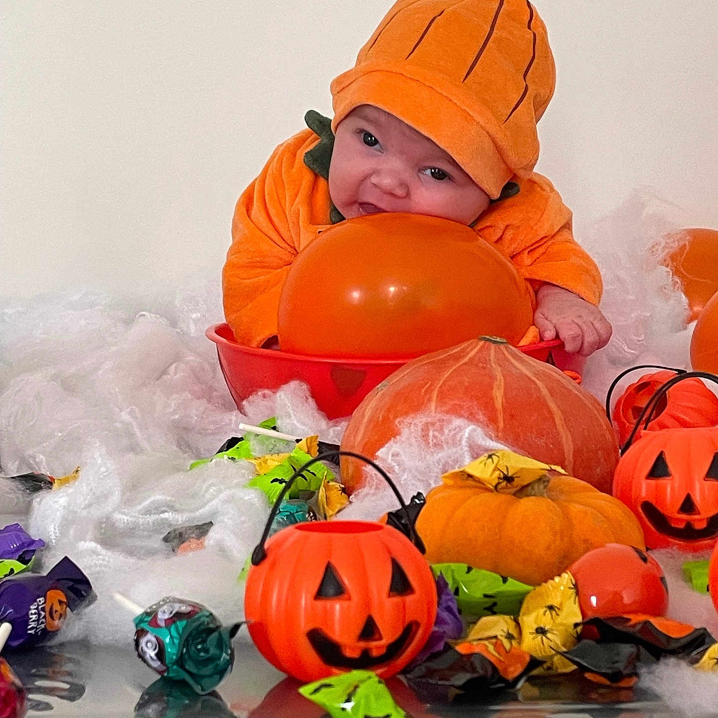Nyna a rejoint le concours — aidez-le/la à gagner de superbes lots ! baby, candy, celebration, costume, cute, decorations, fake_spider_web, festive, green_wrappers, halloween, holiday, infant, orange, orange_balloon, plastic_jack_o_lantern, pumpkin, pumpkin_costume, purple_wrappers, smiling, table