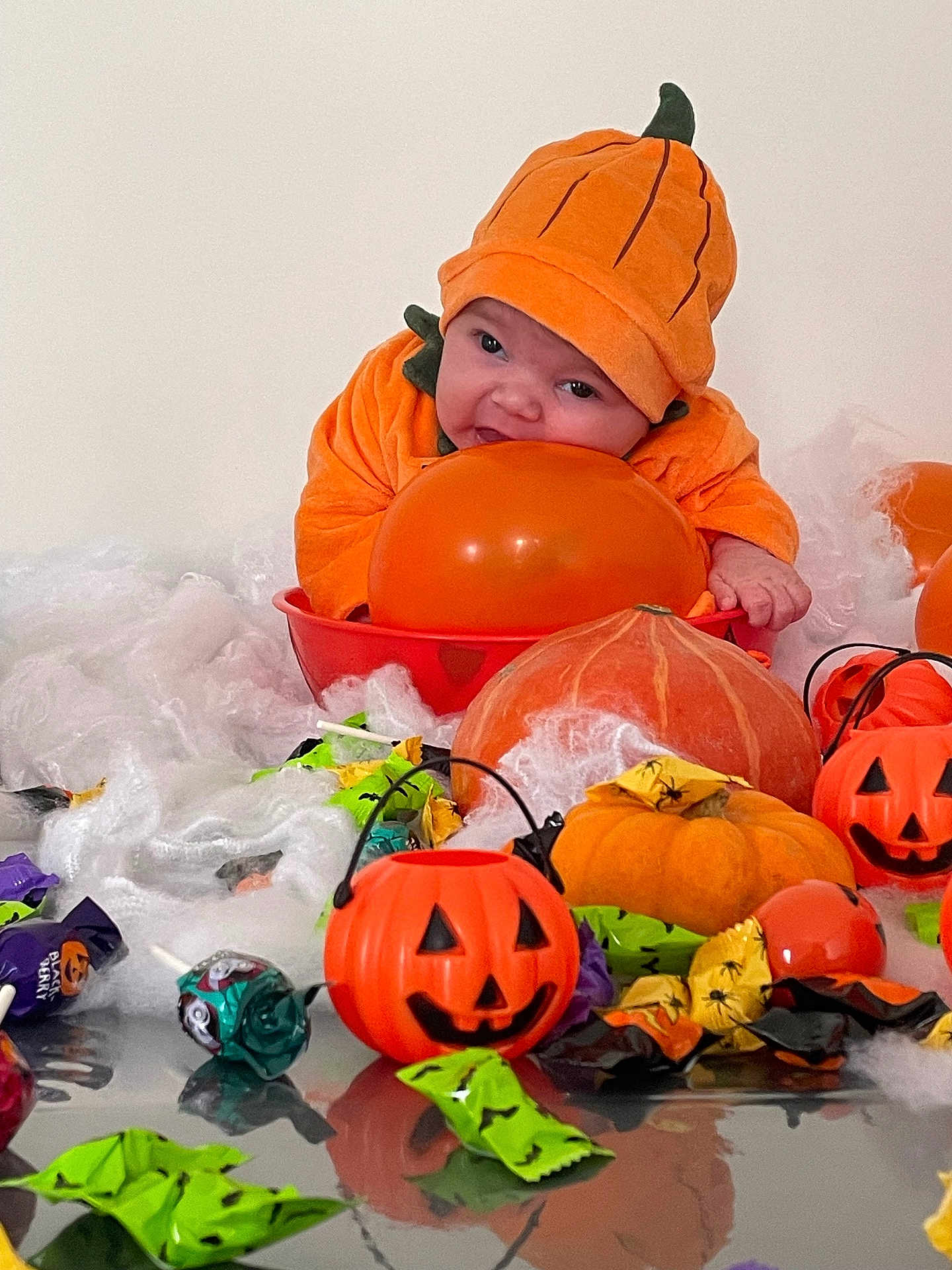 Nyna a rejoint le concours — aidez-le/la à gagner de superbes lots ! baby, pumpkin_costume, orange_balloon, halloween, candy, pumpkin, decorations, fake_spider_web, table, orange, green_wrappers, purple_wrappers, plastic_jack_o_lantern, cute, infant, holiday, celebration, festive, costume, smiling