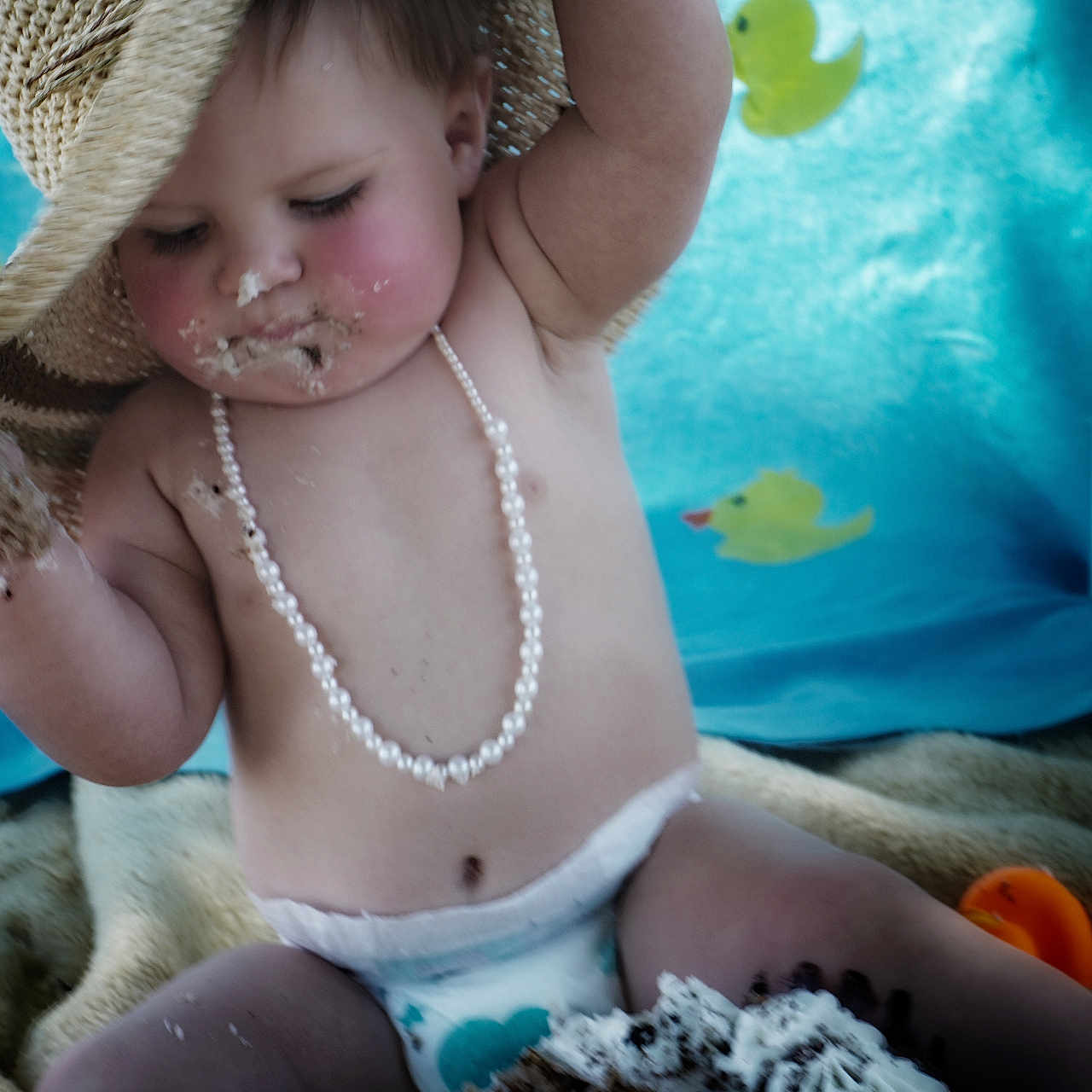 Ellie Mae joined the competition — help win amazing prizes! baby, blue_background, cake, celebration, child, chocolate_cake, cute, diaper, face, food, fun, hat, indoor, messy, pearl_necklace, playful, portrait, sitting, straw_hat, yellow_duck