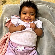 Kataleya joined the competition — help win amazing prizes! baby, smiling, curly_hair, blanket, purple_clothing, white_bow, infant, happy, lying_down, soft_texture, indoors, cute, child, toddler, skin, face, person, hands, closeup, cozy