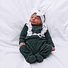 baby, infant, puckered_face, white_bow, headband, green_outfit, lace, cozy_clothing, sitting, soft_blanket, cute_expression, newborn, child, portrait, indoors, adorable, sleepy, small_hands, tiny_feet, comfortable