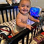 baby, toddler, crib, diaper, smile, child, toy, stuffed_animal, blanket, furniture, nightlight, indoor, bedroom, playful, happy, face, hand, person, clothing, home