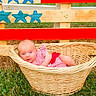 american_flag, baby, basket, blue, child, clothing, cute, daytime, grass, infant, lying_down, nature, outdoor, person, portrait, red, stars, summer, white, wooden_fence