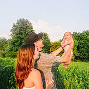Gracelynn Leigh is registered to the contest to win money with this photo: baby, casual_clothing, clouds, family, field, grass, greenery, happy, hat, holding, lifting, man, nature, outdoor, portrait, sky, summer, sunlight, tattoo, woman