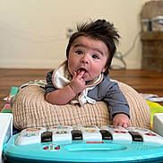 Levi is registered to the contest to win money with this photo: baby, infant, toy_piano, cushion, fingers_in_mouth, indoor, wooden_floor, curious, wild_hair, soft_focus, playtime, child, young, clothing, bib, cute, happy, person, floor, colorful_toy