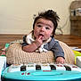 baby, infant, toy_piano, cushion, fingers_in_mouth, indoor, wooden_floor, curious, wild_hair, soft_focus, playtime, child, young, clothing, bib, cute, happy, person, floor, colorful_toy