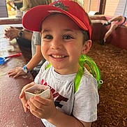 Salim is registered to the contest to win money with this photo: activity, boy, casual_clothing, child, children, container, daylight, friends, fun, green_backpack, happy, outdoor, playground, red_cap, rocks, smiling, summer, table, white_shirt, wood_chips