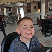 Anael a rejoint le concours — aidez-le/la à gagner de superbes lots ! child, boy, smile, haircut, salon, barbershop, steering_wheel, chair, interior, tiles, person, mirror, cabinet, hair_washing_station, clothing, floor, door, lighting, happy, casual