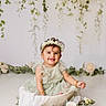 baby, celebration, child, cute, decorative, dress, floral_crown, flowers, garden, greenery, happy, indoors, infant, portrait, rustic_bowl, seated, smiling, studio_photography, vines, white_clothing