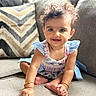 baby, barefoot, blue_eyes, bracelets, child, couch, cozy, curly_hair, dress, floral_clothing, happy, home, indoor, infant, photography, pillow, portrait, sitting, smiling, sofa