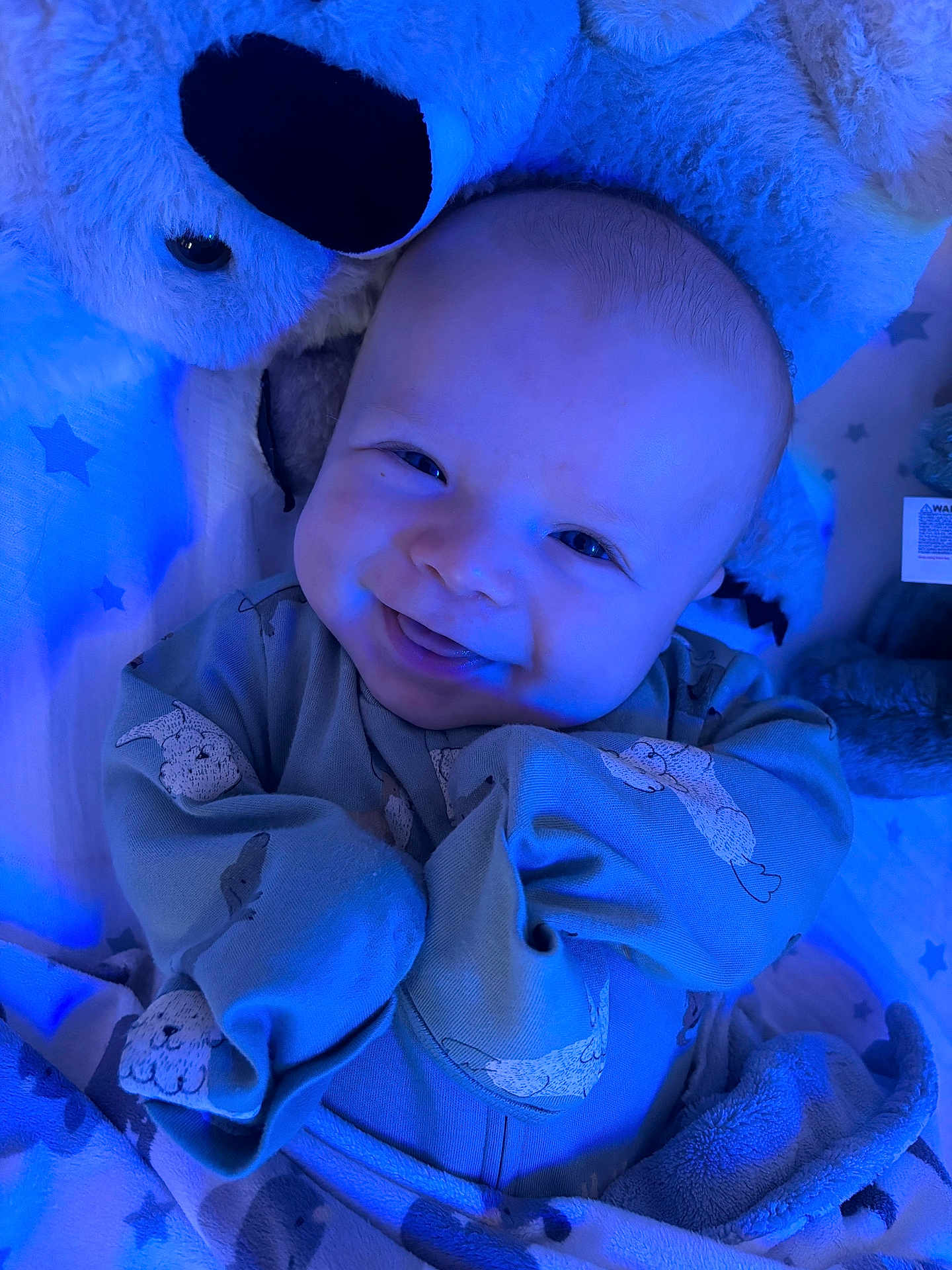 Eastyn is registered to the contest to win money with this photo: baby, smiling, onesie, plush_bear, blue_light, blanket, cute, infant, cozy, sleepwear, soft_toys, happy, child, portrait, indoors, lying_down, face, warm, comfort, newborn
