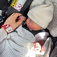Eastyn is registered to the contest to win money with this photo: baby, infant, car_seat, blanket, hat, hand, adult_hand, finger, safety_warning, clothing, sleeping, child, newborn, seatbelt, pattern, striped_hat, closeup, indoor, resting, transport
