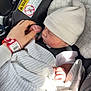 baby, infant, car_seat, blanket, hat, hand, adult_hand, finger, safety_warning, clothing, sleeping, child, newborn, seatbelt, pattern, striped_hat, closeup, indoor, resting, transport