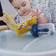 Luke joined the competition — help win amazing prizes! toddler, child, book, reading, high_chair, sippy_cup, indoor, furniture, face, curly_hair, expression, table, tray, toy, deer_skull, antlers, living_room, clothing, person, bilingual