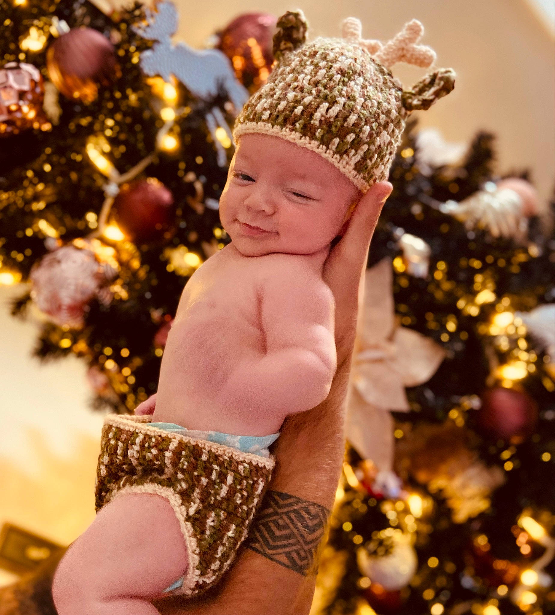 Keaton is registered to the contest to win money with this photo: baby, branch, cap, christmas, christmas_decoration, christmas_eve, christmas_ornament, christmas_tree, eye, fawn, finger, fun, gesture, hand, happy, headwear, holiday_ornament, ornament, people_in_nature, person