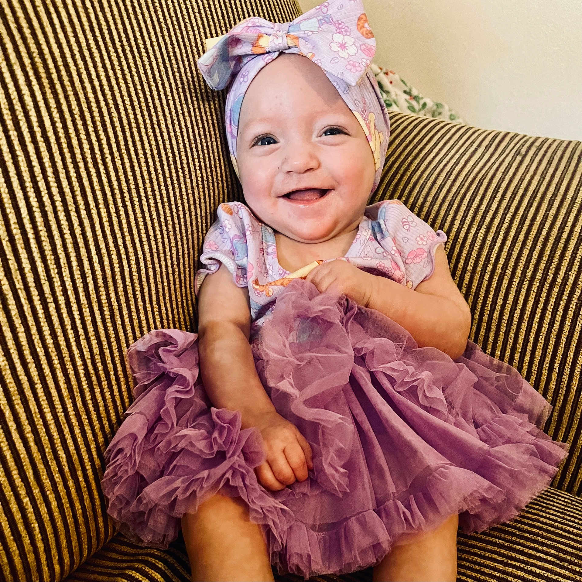 Jayla joined the competition — help win amazing prizes! baby, bow, child, clothing, couch, cute, dress, face, hand, happy, headband, indoors, infant, person, portrait, purple, sitting, smile, striped, toddler