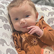 Rose joined the competition — help win amazing prizes! baby, infant, smile, face, blue_eyes, brown_clothing, flower_pattern, hedgehog_patch, elephant_pattern, pillow, soft_focus, hand, cute, portrait, lying_down, cozy, child, young, indoors, warm_colors