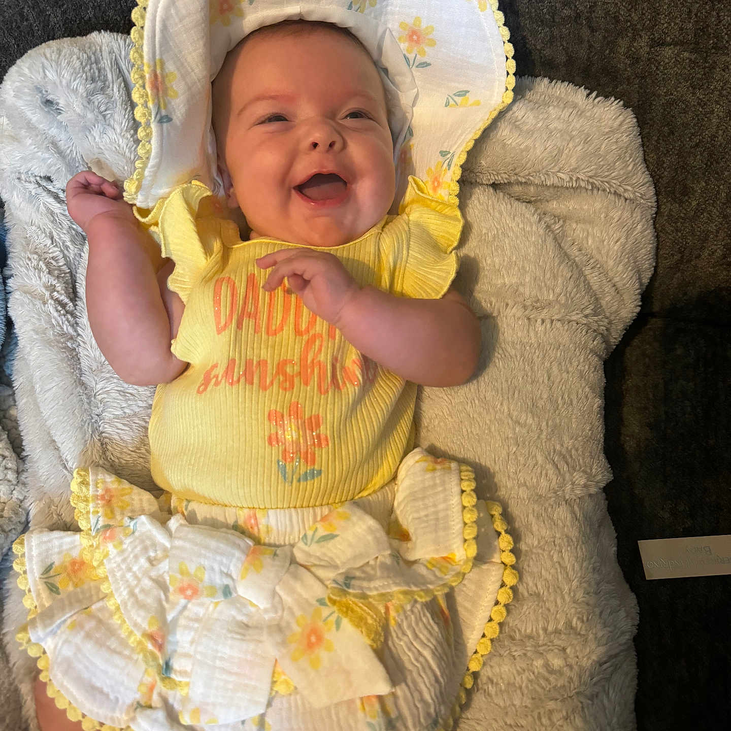 Taylor is registered to the contest to win money with this photo: baby, baby_girl, blanket, bonnet, cheerful, child, clothing, comfort, cozy, cute, floral_pattern, happy, indoors, infant, lying_down, portrait, smiling, soft_texture, toddler, yellow_outfit