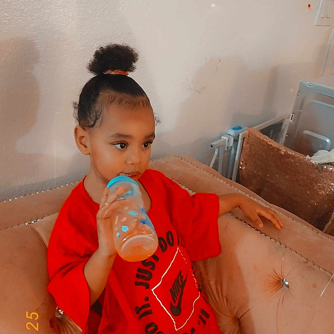Deylani joined the competition — help win amazing prizes! baby_bottle, casual, child, comfortable, couch, cozy, curly_hair, cute, drinking, furniture, home, indoor, nike_logo, person, portrait, red_shirt, relaxed, sitting, toddler, young_child