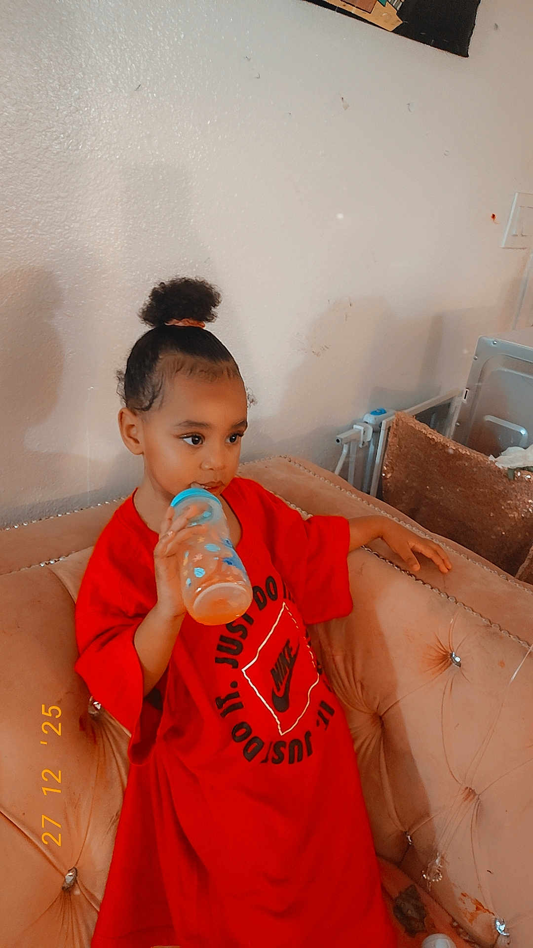 Deylani joined the competition — help win amazing prizes! toddler, child, baby_bottle, red_shirt, nike_logo, couch, indoor, curly_hair, sitting, drinking, relaxed, casual, young_child, furniture, home, portrait, person, comfortable, cozy, cute