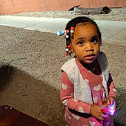 Deylani joined the competition — help win amazing prizes! child, girl, braided_hair, beads, pink_dress, heart_pattern, vest, toy, glowing, night, outdoor, table, corned_beef, packaged_food, sidewalk, gravel, shoes, curious, looking_up, person