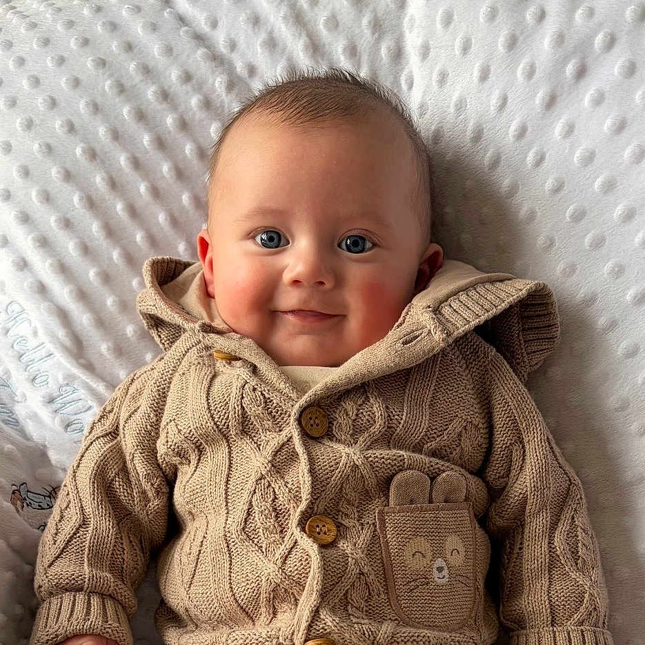 Elio is registered to the contest to win money with this photo: baby, baby_clothes, baby_face, beige_clothing, blue_eyes, buttoned_jacket, cheeks, child, cozy, cute, cute_expression, happy, indoor, infant, knitted_sweater, portrait, smile, soft_blanket, texture, warm