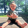 Zeke is registered to the contest to win money with this photo: toddler, child, outdoor, picnic_table, hat, cap, grass, trees, lake, sunlight, summer, baby, holding, sign, wooden, nature, smiling, casual_clothing, barefoot, park